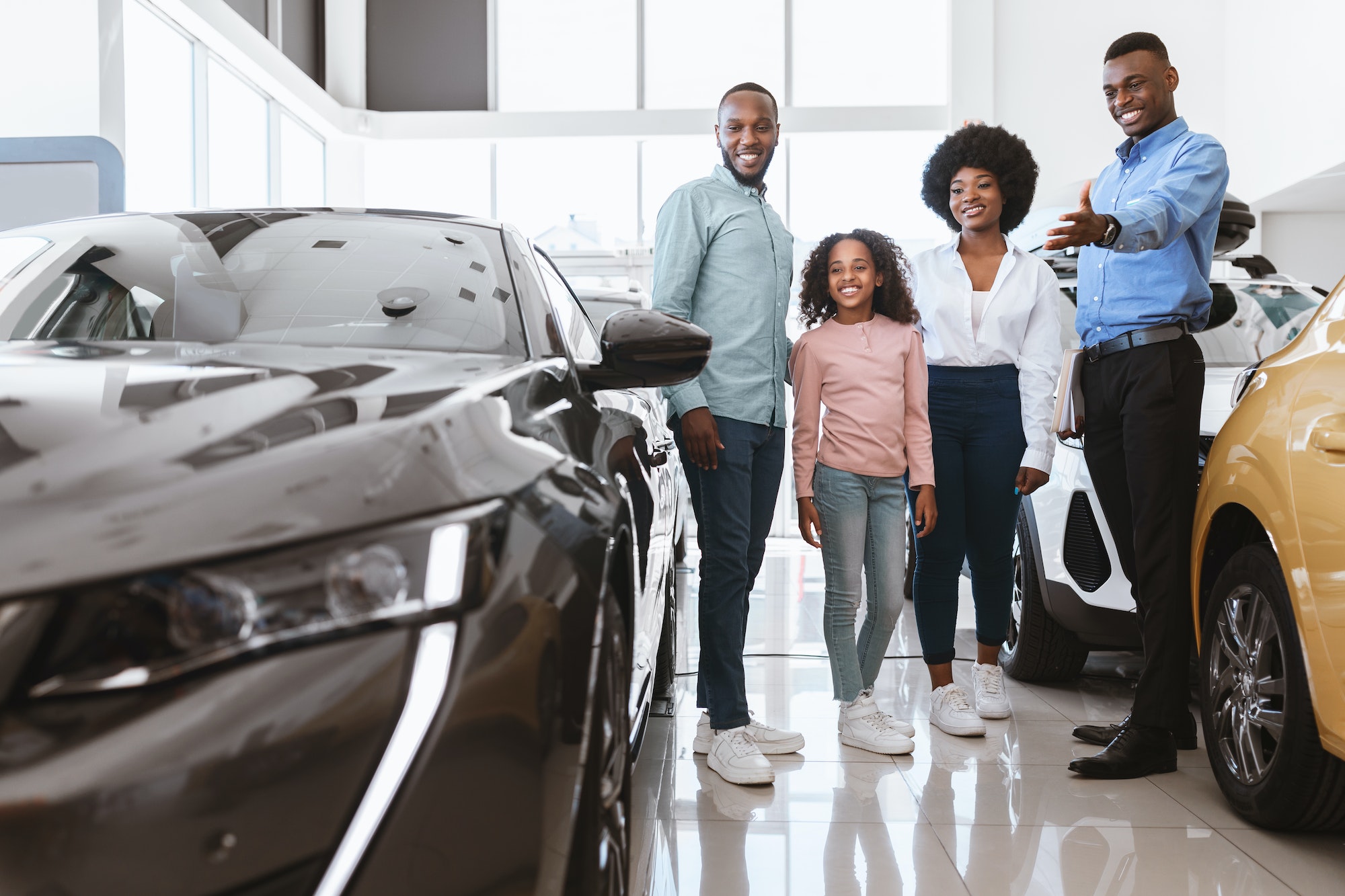 Car purchase or rental. Joyful black family talking to smiling salesman about buying new auto at